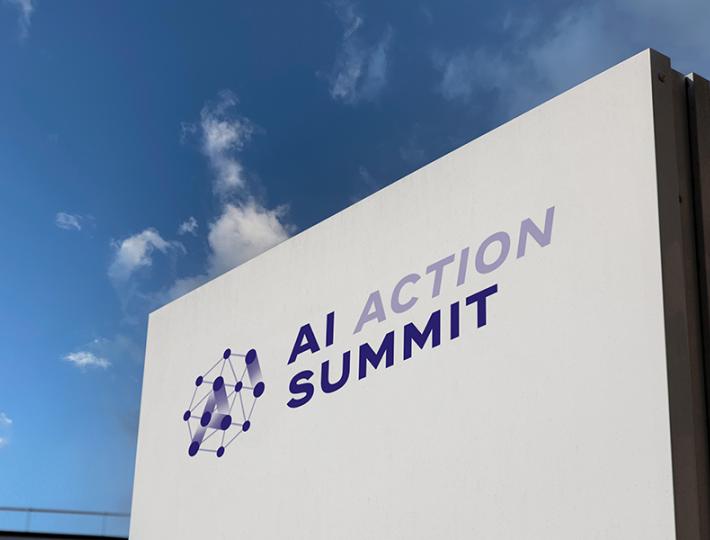 A large white sign for the AI Action Summit against a blue sky.